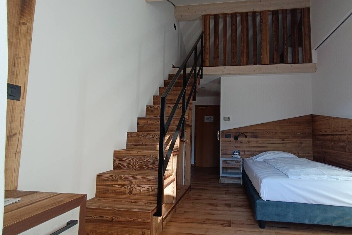 A bedroom with a wooden staircase, a bed, and a small bedside table.