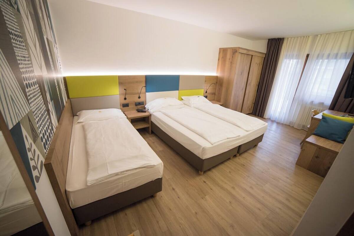 A hotel room with two single beds, a wooden wardrobe, a nightstand, and a small seating area.
