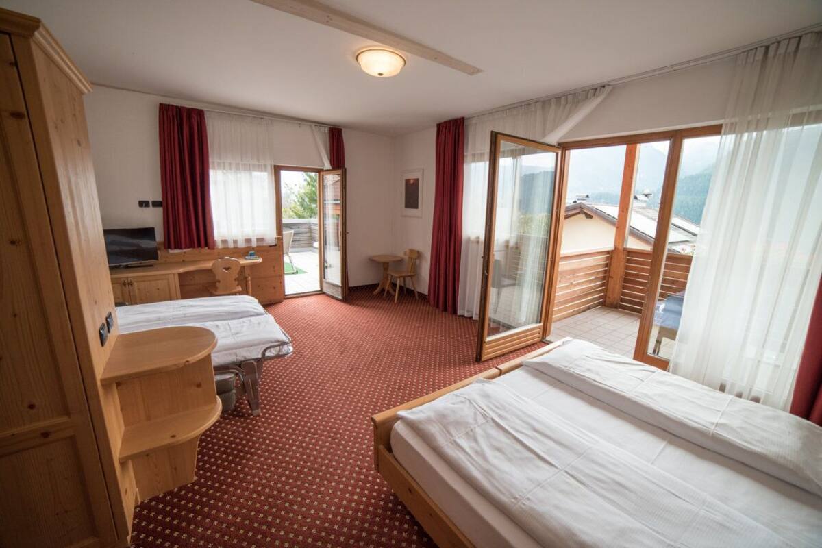 A hotel room with two beds, a desk, a chair, and a large sliding glass door to a balcony.