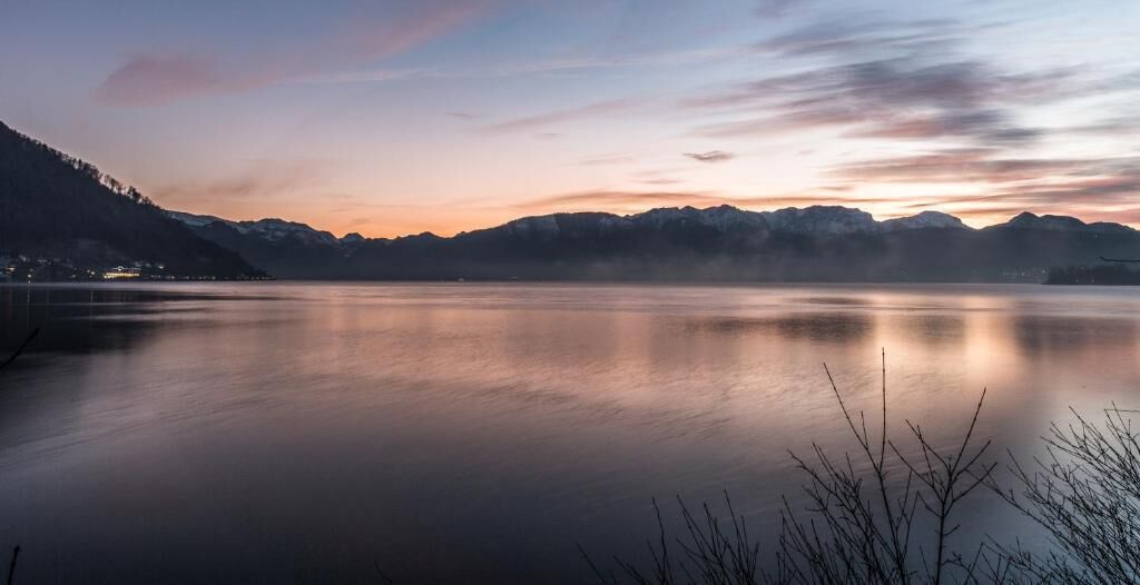 Un lago tranquilo con montañas al fondo y un cielo despejado.