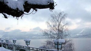 A snow-covered outdoor area with a metal fence and street lamps, overlooking a body of water and mountains. - Landhotel Gasthof Grunberg (Gmunden)
