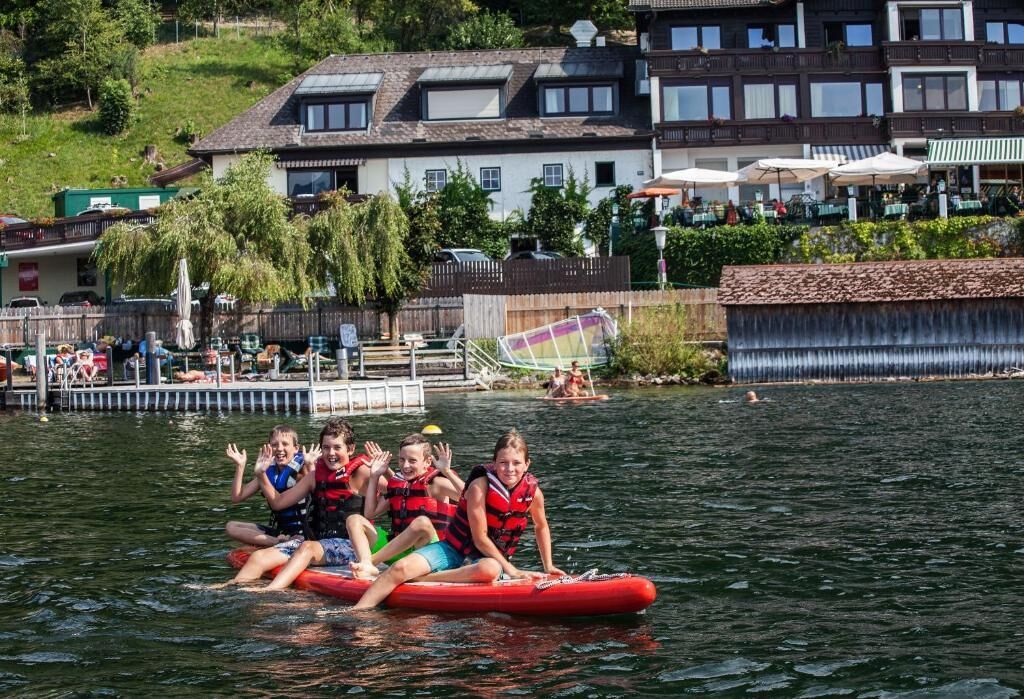 A group of people on a red raft in a lake with a wooden dock and buildings in the background.