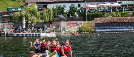 A group of people on a red raft in a lake with a wooden dock and buildings in the background.