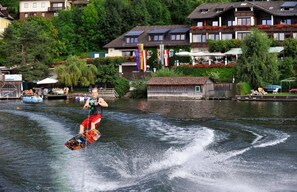 Una persona practicando wakeboard en un río, con casas y árboles al fondo.