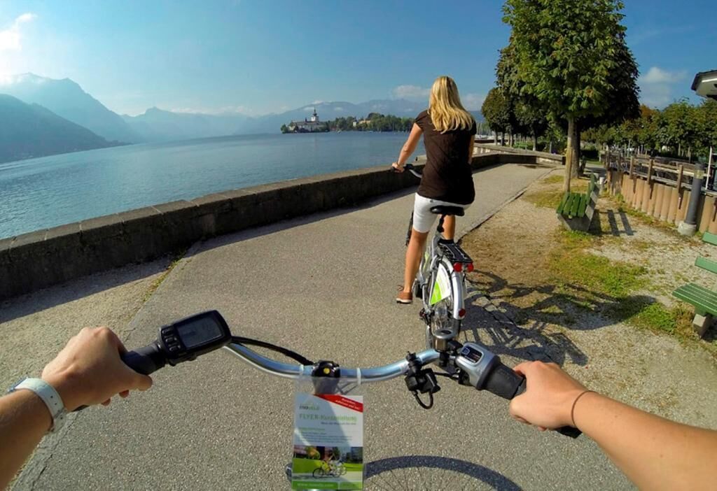 A paved path alongside a body of water with a cyclist and a person standing by the water.