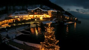 A hotel with a waterfront view, a snow-covered deck, and a lit Christmas tree. - Landhotel Gasthof Grunberg (Gmunden)