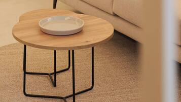 A modern living room with a beige sofa, a round wooden coffee table with a white plate, and a black metal base.