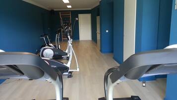 Une salle de sport équipée de tapis de course, de vélos elliptiques et d’un appareil d’escalier.
