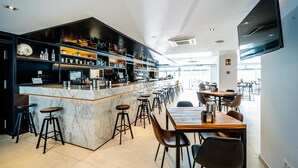 A modern bar area with a marble counter, stools, and a flat-screen TV mounted on the wall.