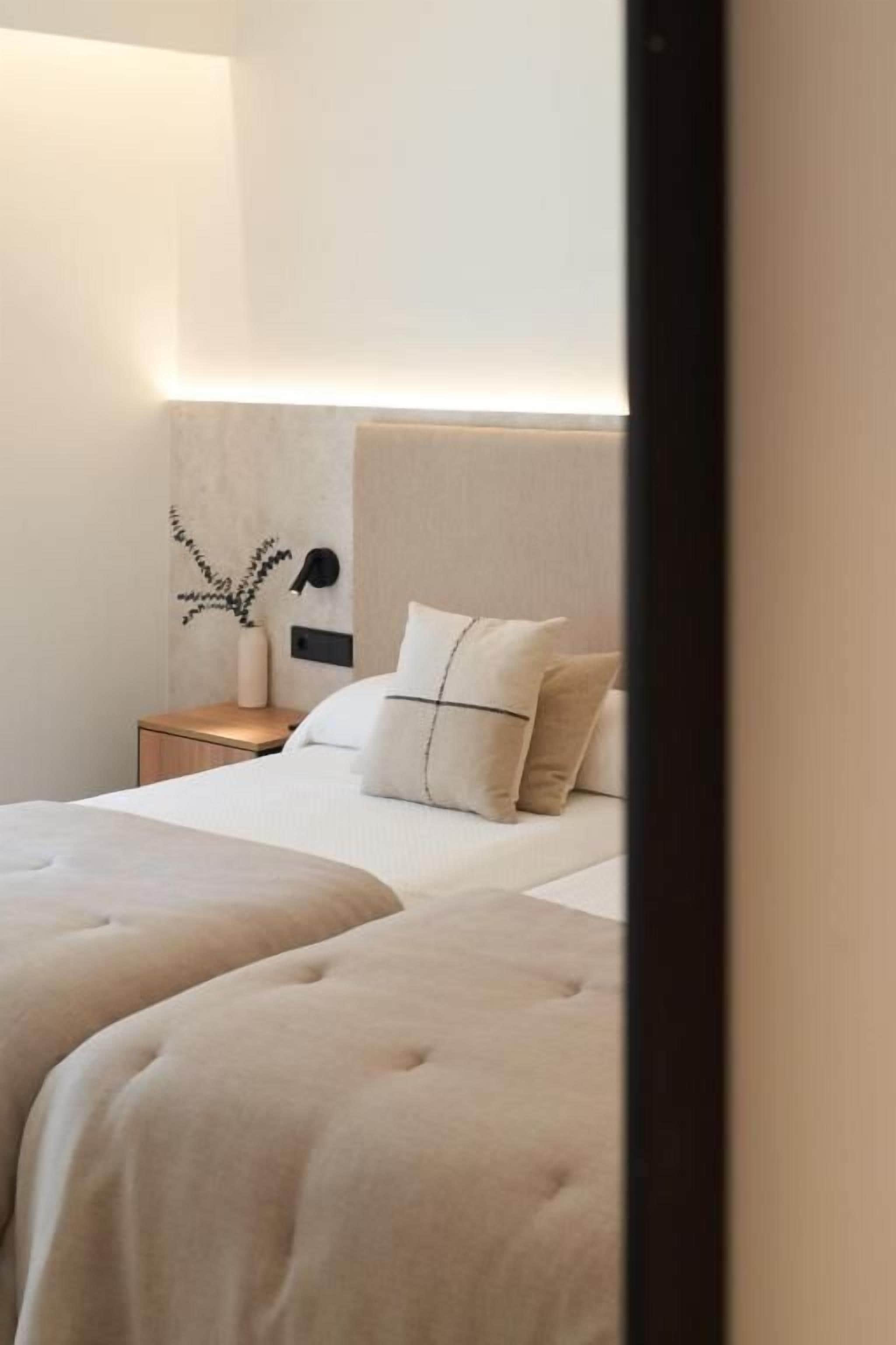 A hotel room with two beds, a nightstand, and a wall-mounted lamp.