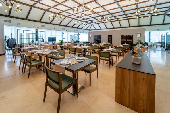 Un comedor amplio con varias mesas y sillas, una barra central y ventanas grandes que dejan entrar luz natural.