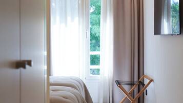 Un dormitorio con cama, televisión instalada en la pared y ventana con cortinas.