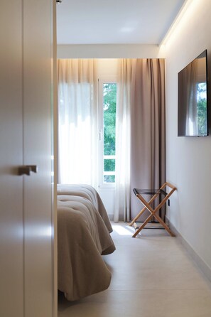 A bedroom with a bed, a TV mounted on the wall, and a window with curtains. - Jardines La Tejera (Olula Del Rio)