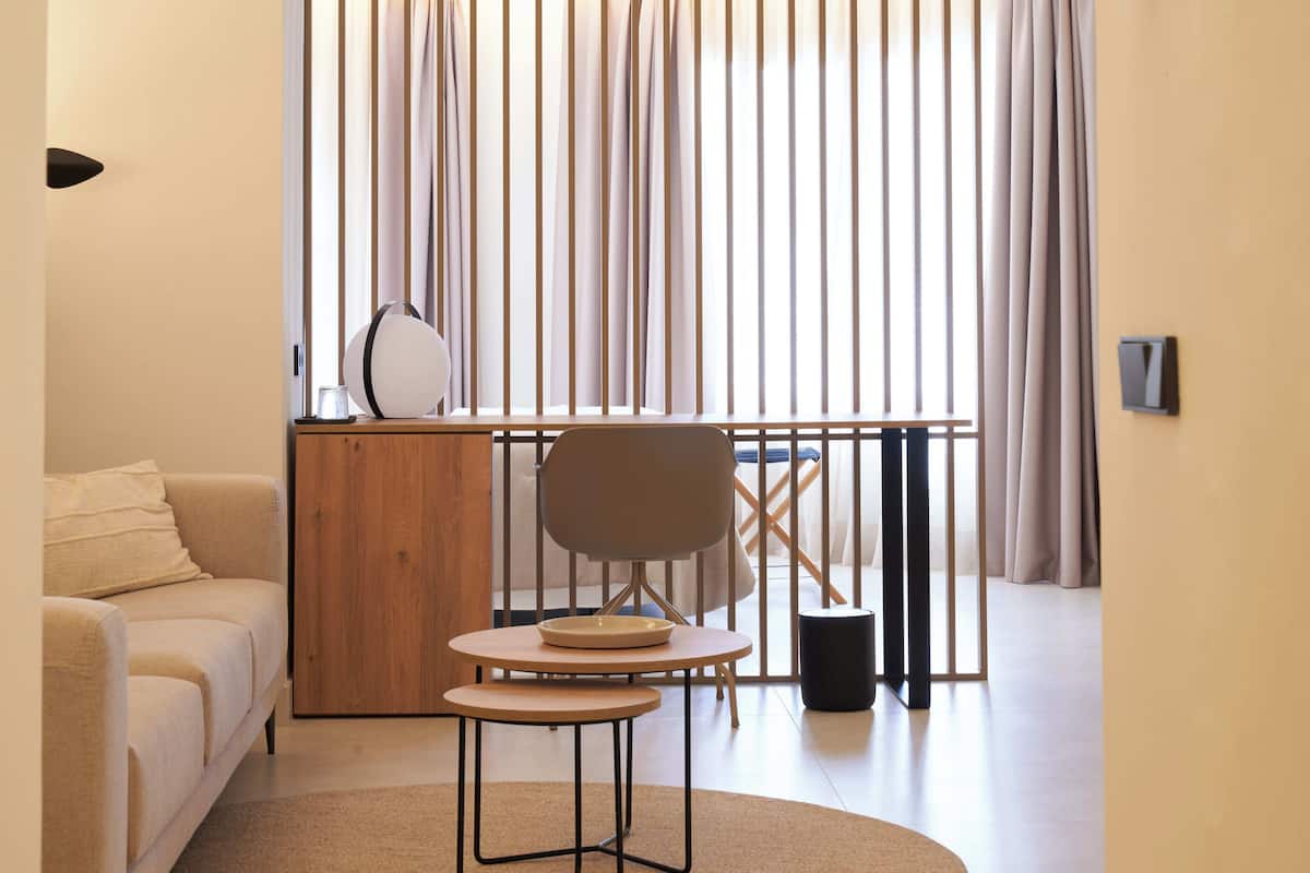 A modern living room with a sofa, a round table, and a chair. There is a wooden cabinet and a black trash bin.