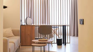 Een moderne woonkamer met een bank, een ronde tafel en een stoel. Er is een houten kastje en een zwarte prullenbak.
