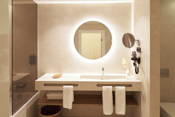 Un baño moderno con un espejo redondo, dos lavamanos, una ducha y un perchero para toallas.