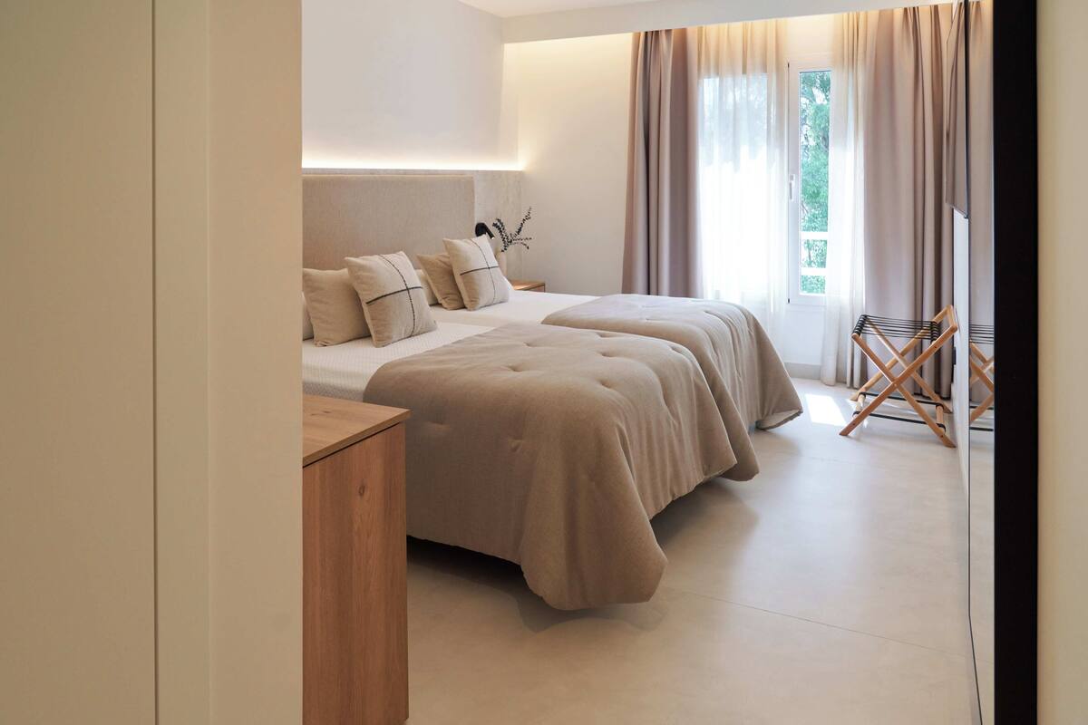 A modern hotel room with two beds, a wooden nightstand, and a window with curtains.