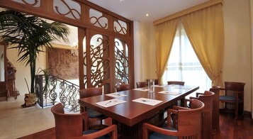 Una sala conferenze con un lungo tavolo di legno, diverse sedie e un pannello decorativo.