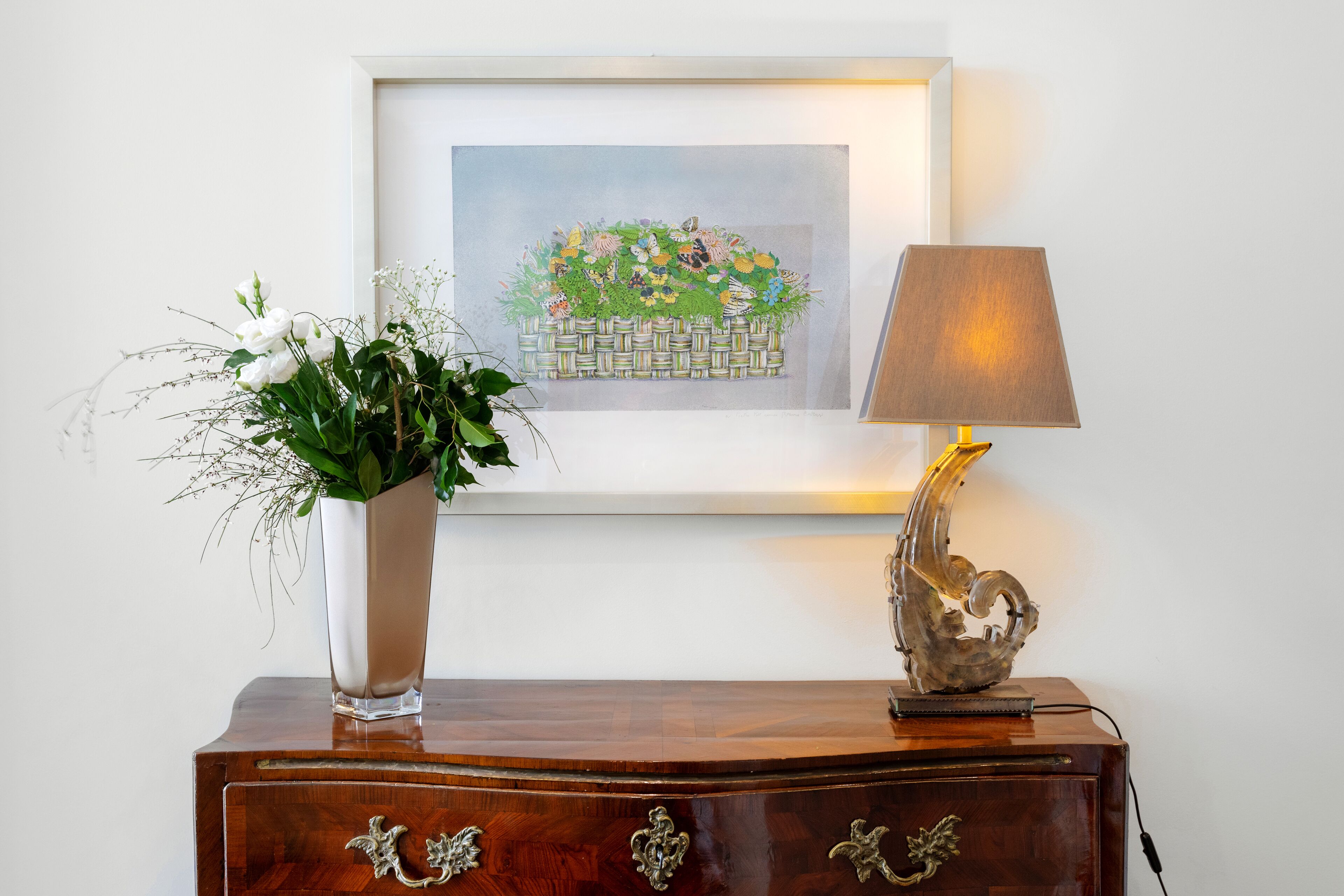 A wooden dresser with a vase of white flowers and a framed artwork above it.