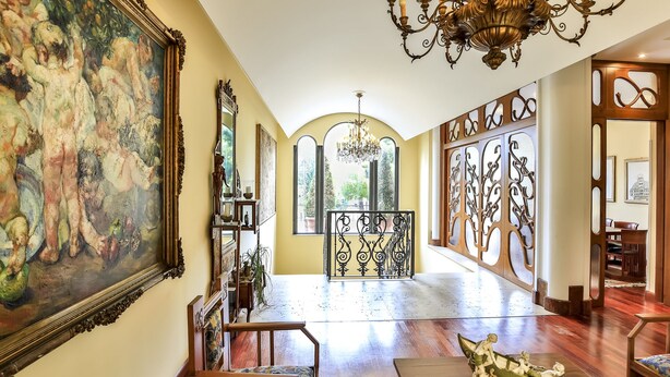 A spacious hallway with a large painting, ornate chandeliers, and a view through a window. - Hotel Giardino Inglese (Palermo)