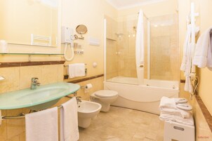 Un bagno moderno con lavabo in vetro, un water, un bidet, una vasca da bagno e una cabina doccia in vetro.