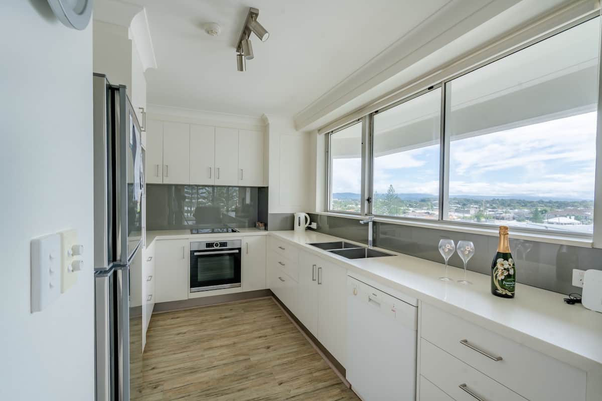 Una cocina moderna con armarios blancos, horno empotrado, un ventanal con vista a la ciudad y una botella de champán sobre la encimera.