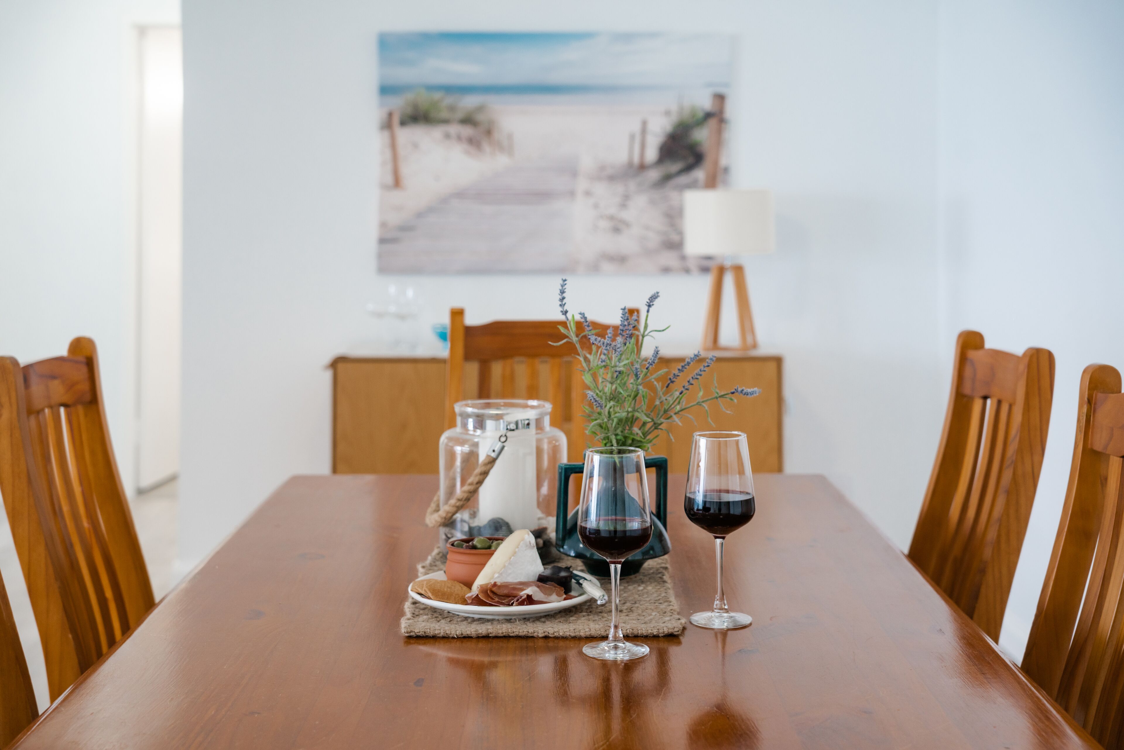 Een houten eettafel met een bord eten, een glas rode wijn en een vaas lavendel.