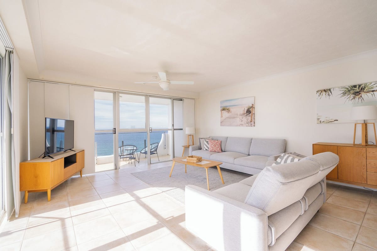 Amplia sala de estar con sofá, televisión y balcón con vistas al mar.