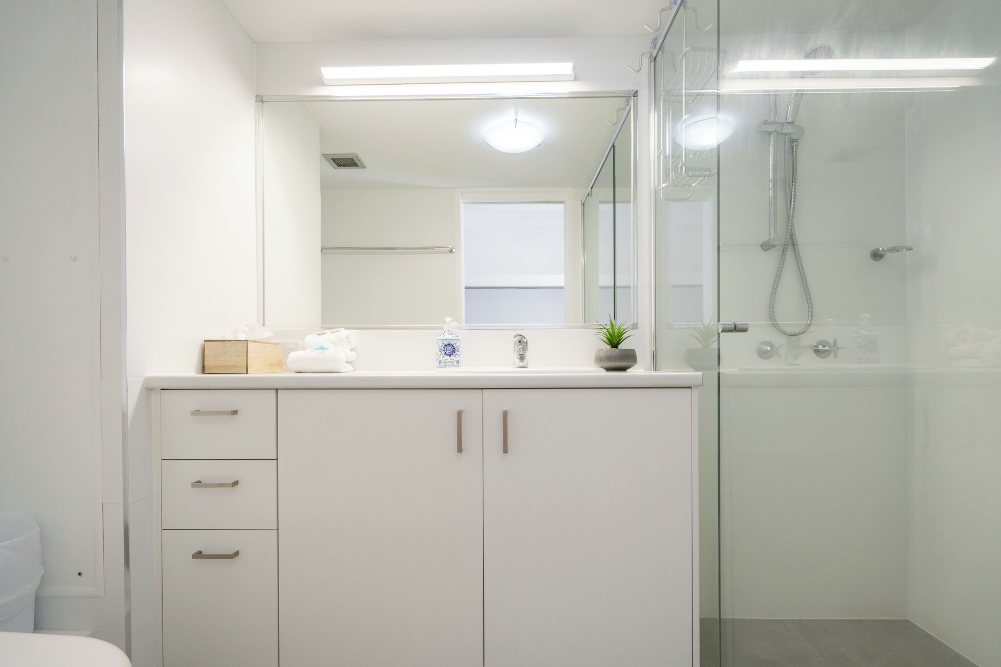 A modern bathroom with a glass shower enclosure, a white vanity with drawers, and a mirror above the sink.