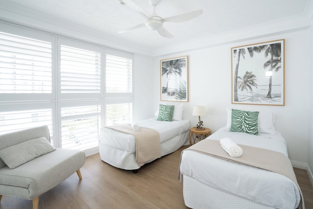 Habitación de hotel con dos camas, un sofá y ventanas amplias con persianas.