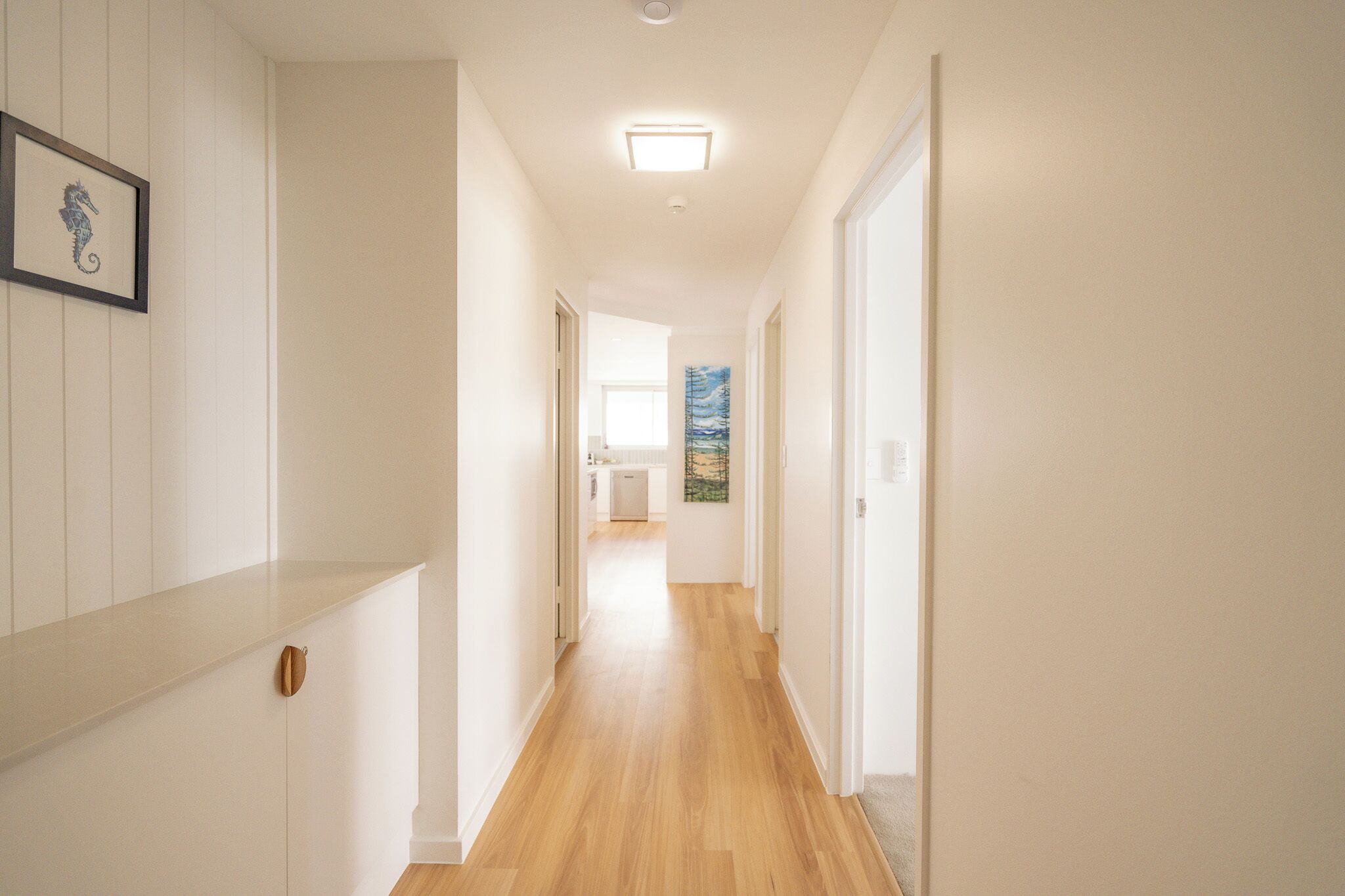 A hallway with wooden flooring, white walls, and a framed seahorse artwork.