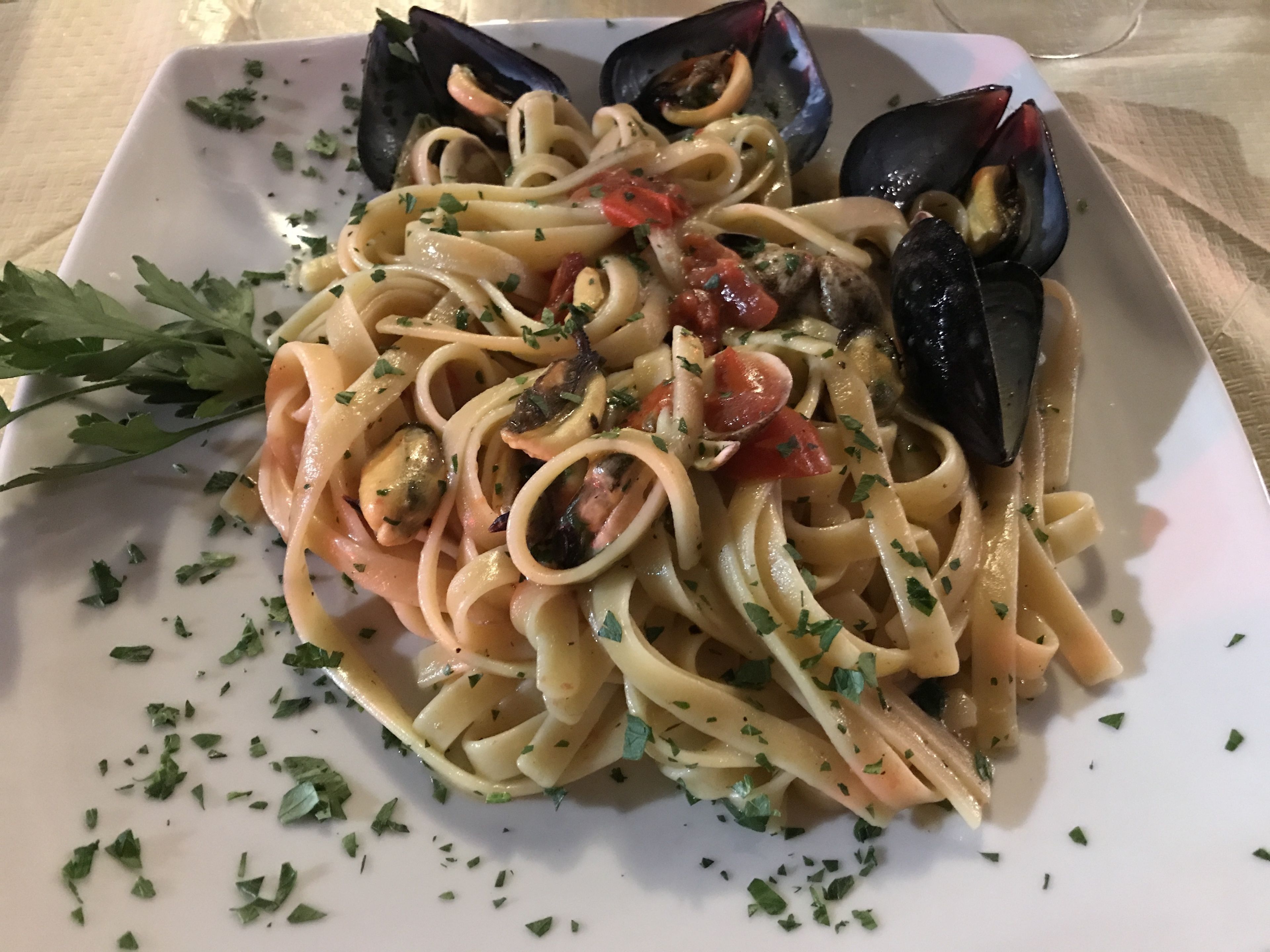 Lautasellinen pastaa, jossa on simpukoita, tomaatteja ja persiljaa.