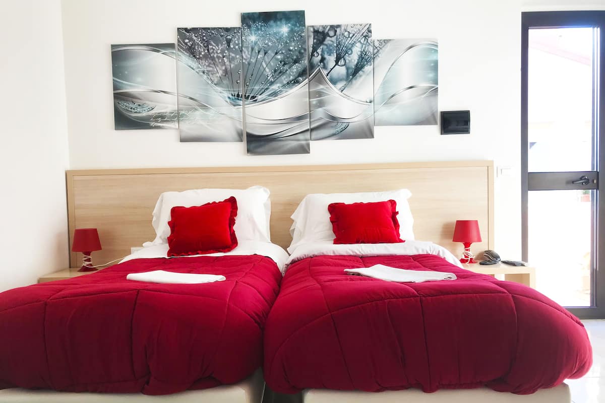 A double bed with red bedding, two red pillows, and a nightstand with a red lamp.