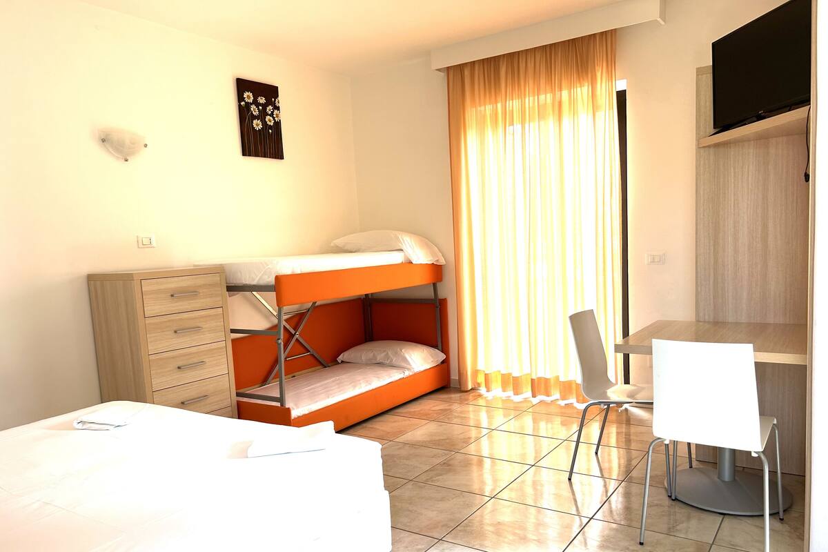 A dormitory room with a bunk bed, a desk, a chair, and a dresser.