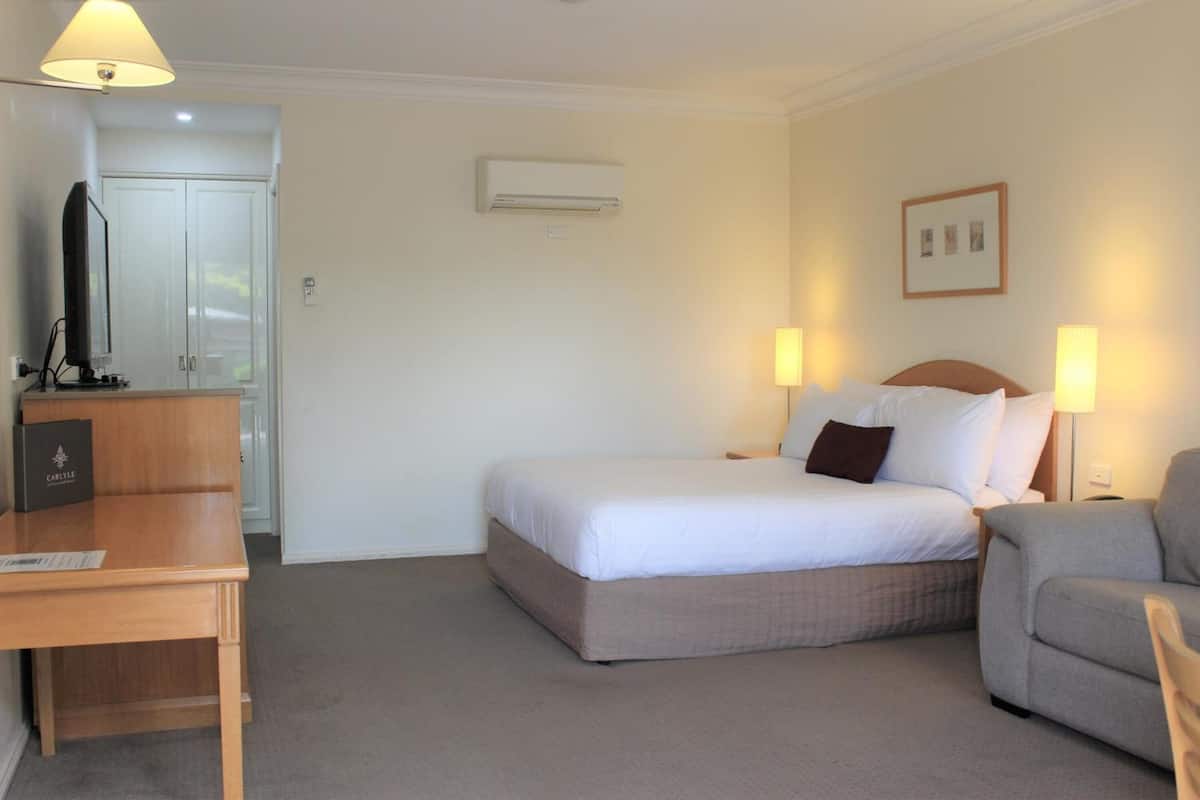 A hotel room with a bed, bedside lamps, a desk, a television, and an air conditioning unit.