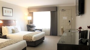 A hotel room with two beds, a desk, a chair, a TV, and a window with curtains.