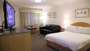 A hotel room with a bed, a desk with a television, a leather sofa, a chair, and a lamp.