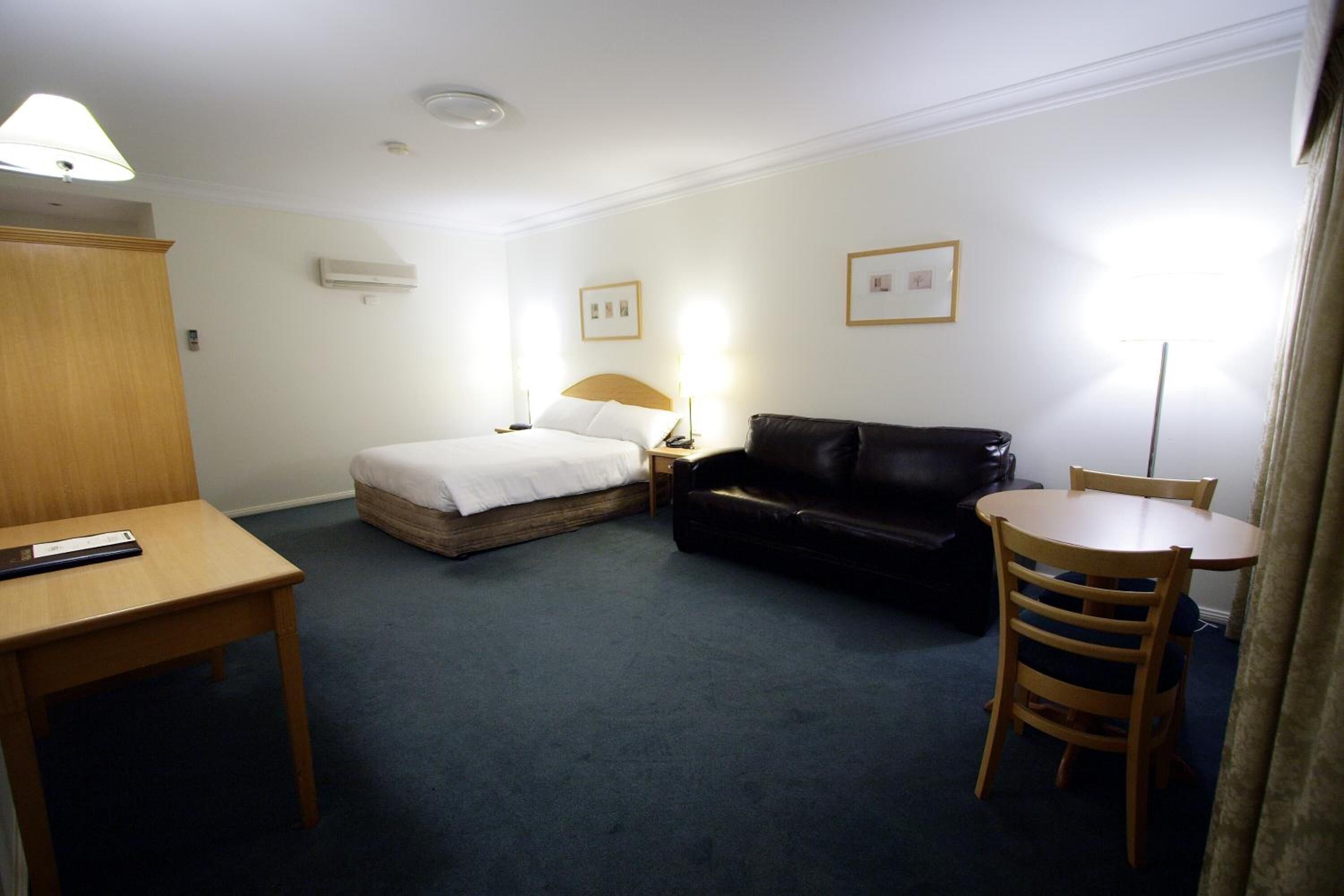 Ett hotellrum med en säng, en svart lädersoffa, ett träbord och ett litet runt bord med en stol.