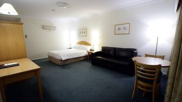 Ett hotellrum med en säng, en svart lädersoffa, ett träbord och ett litet runt bord med en stol.