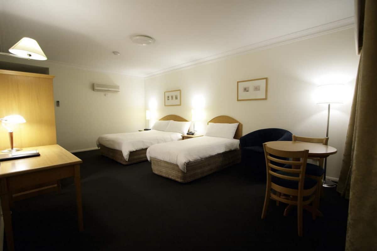 A hotel room with two single beds, a desk with a lamp, a chair, and a small table.