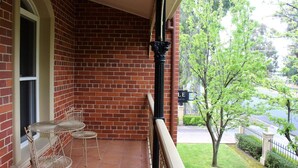 A brick building with a balcony, a table and chairs, and a view of a tree and street.
