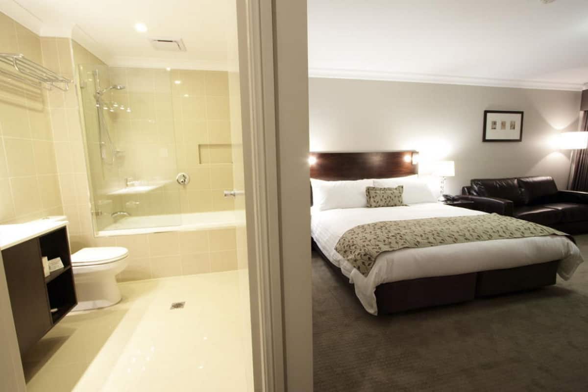 A hotel room with a large bed, a bedside table, a lamp, a shower area, and a toilet.