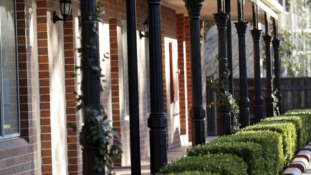 A building with a brick facade, black columns, and a neatly trimmed hedge.