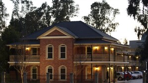 A two-story brick building with a balcony on the upper floor, a covered front porch, and a parking area with cars.