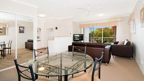 A modern living room with a glass dining table, brown leather sofa, and a television. - Champelli Palms (Labrador)