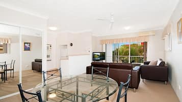 Uma sala de estar moderna com uma mesa de jantar de vidro, sofá de couro marrom e uma televisão.
