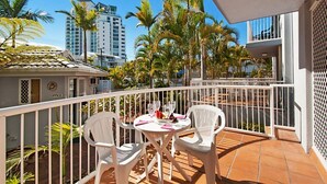 A balcony with white chairs and a table, surrounded by palm trees and a cityscape in the background. - Champelli Palms (Labrador)