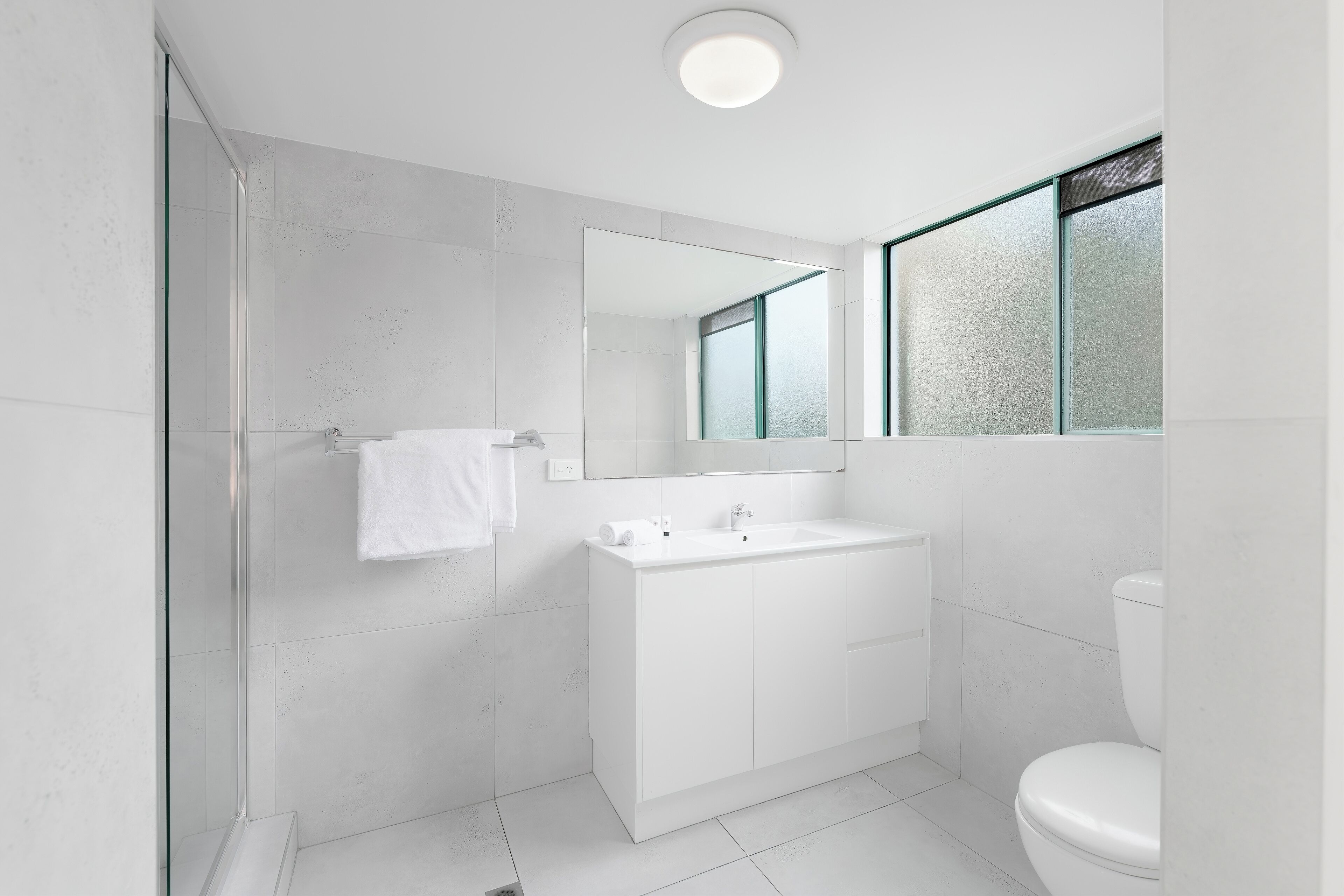 Et moderne badeværelse med en glasbrusekabine, en hvid vask og et toilet.
