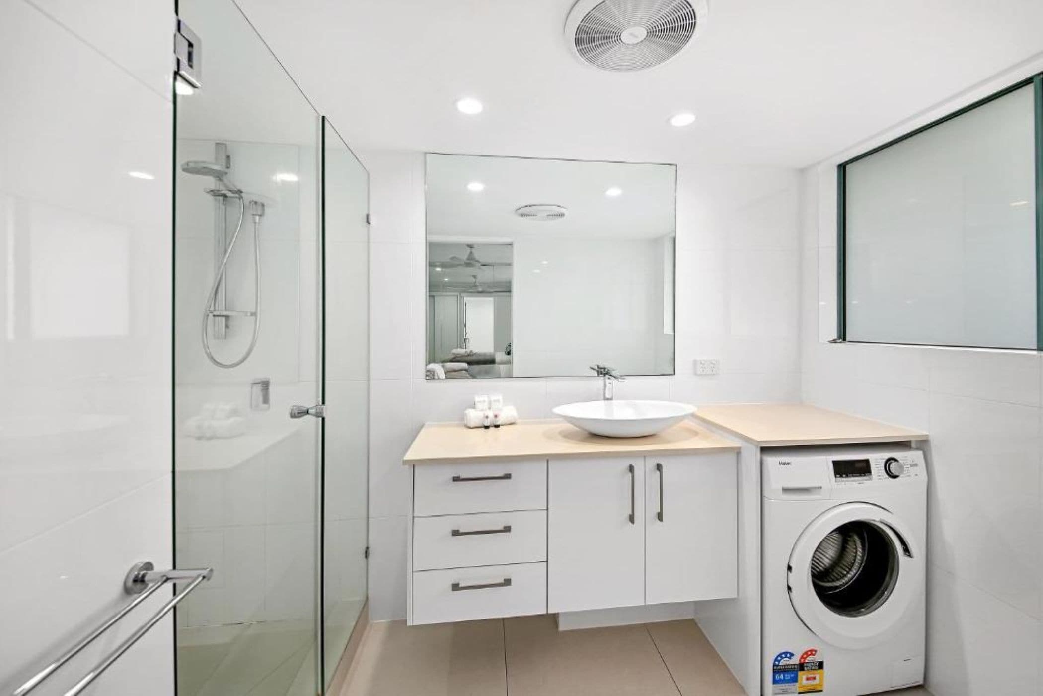 A modern bathroom with a glass shower enclosure, a sink with a mirror above, and a built-in washing machine.
