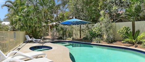 Un patio trasero con piscina, dos sillones de descanso y una sombrilla azul.